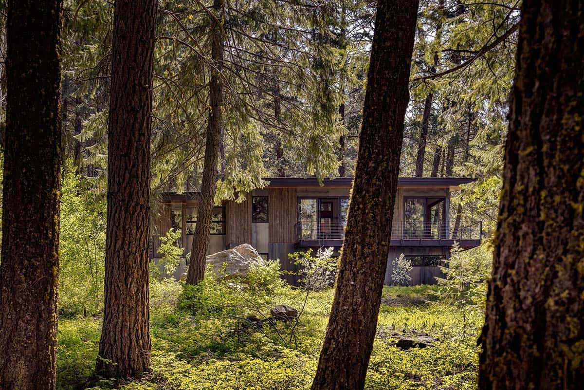 Modern hillside house glimpsed through forest trees with large boulder and cable railing deck
