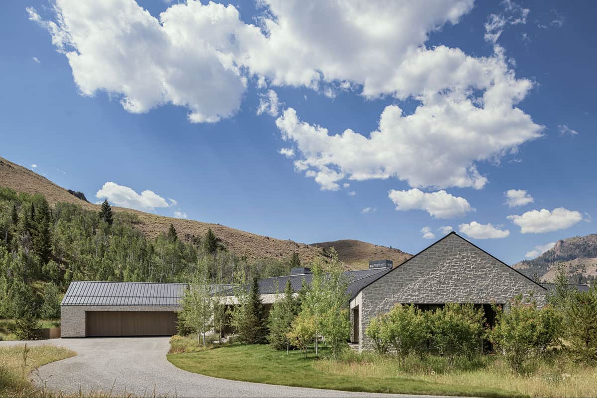 Modern stone and timber house nestled against mountain foothills with circular gravel driveway
