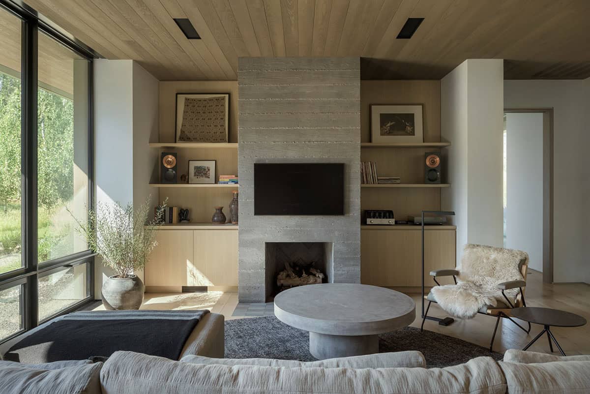 Living room with board-formed concrete fireplace, built-in oak shelving, and floor-to-ceiling windows
