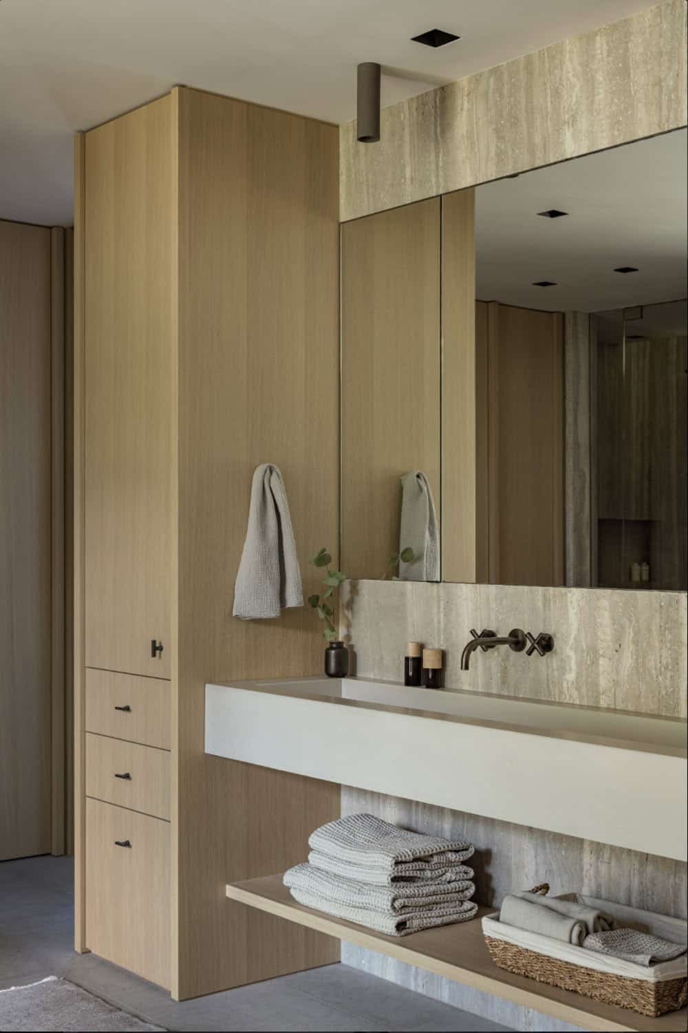 Bathroom vanity with floating concrete sink, travertine backsplash, and oak storage cabinet