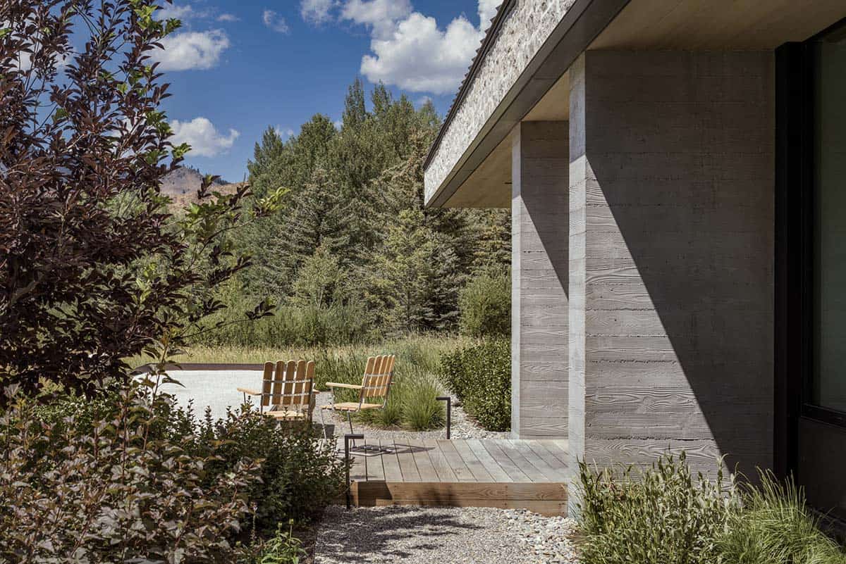Covered patio with board-formed concrete column overlooking meadow and Adirondack chairs