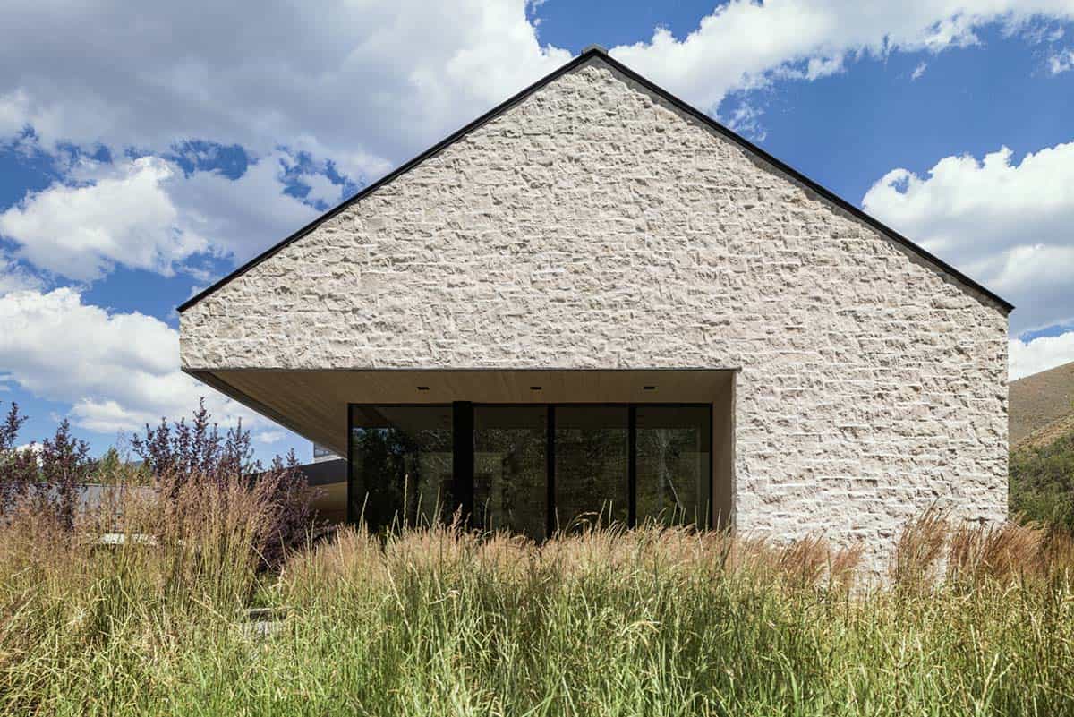 Gabled stone facade with cantilevered roof shading a wall of black-framed windows
