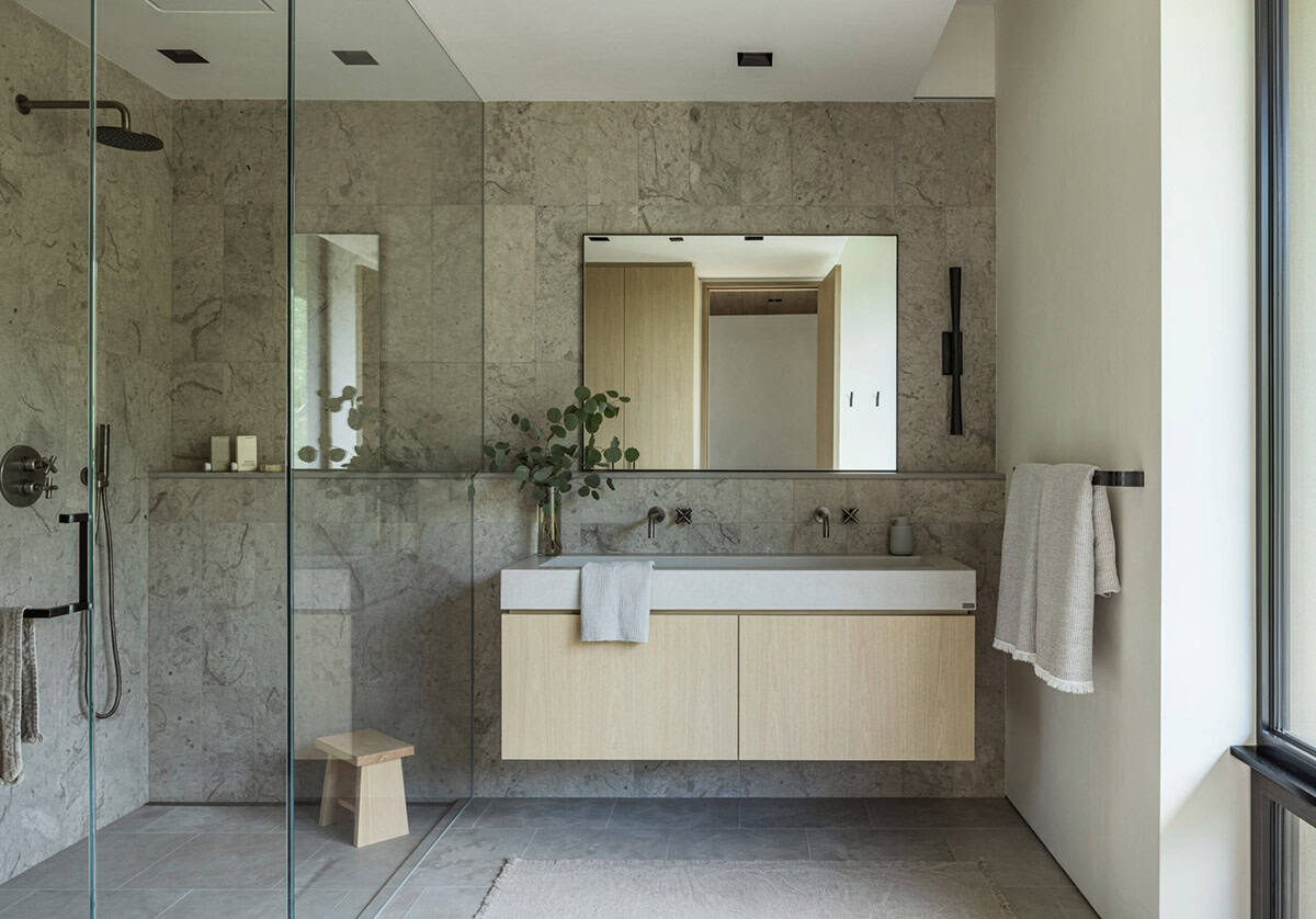 Bathroom with stone-tiled walk-in shower, floating oak vanity, and dual wall-mounted faucets