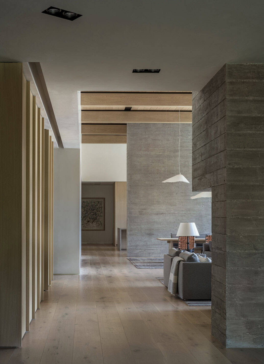 Hallway with wood slat wall leading toward a board-formed concrete fireplace and living area