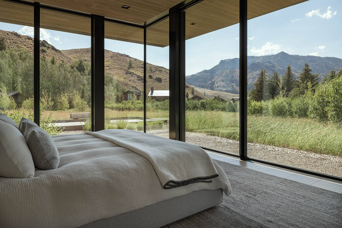 Bedroom with floor-to-ceiling corner windows framing mountain and meadow views