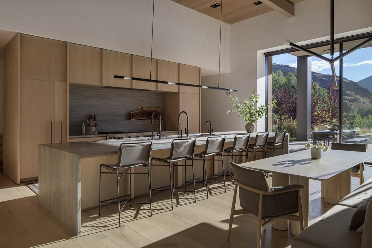 Open kitchen with long oak island, bar stools, and mountain view through glass doors