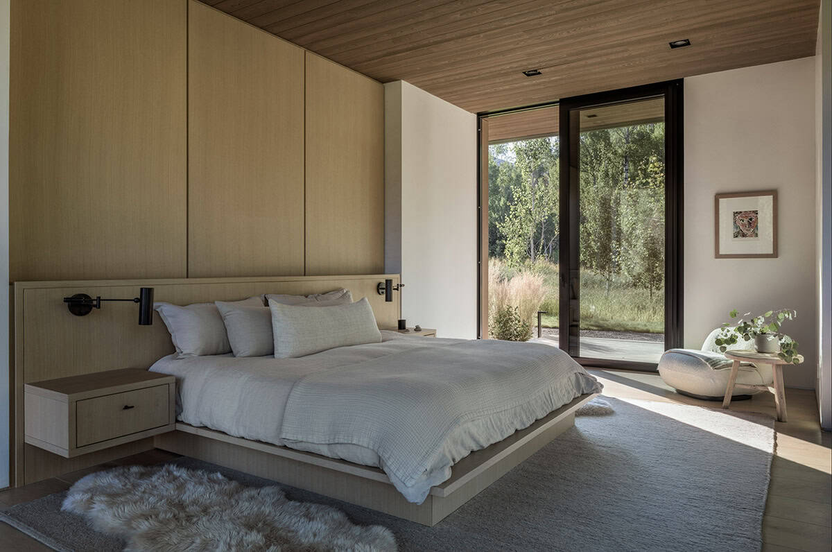 Bedroom with an oak paneled headboard, wall and a sliding glass door to a wooded yard