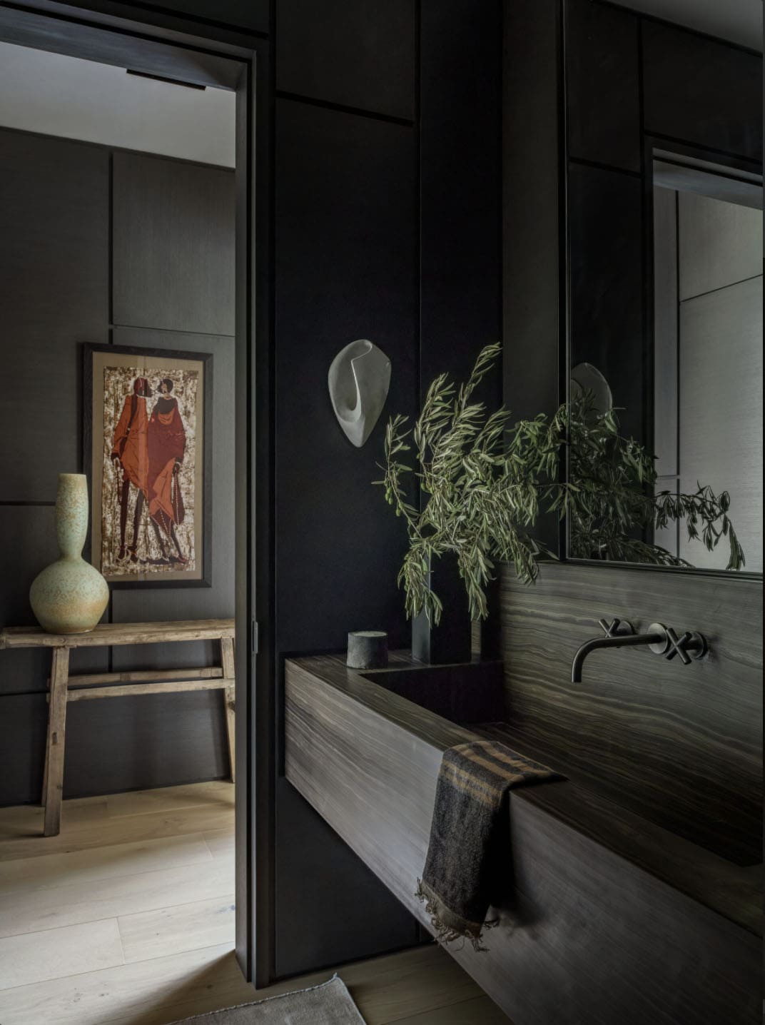 Dark moody powder room with wood-grain stone vanity and olive branch arrangement