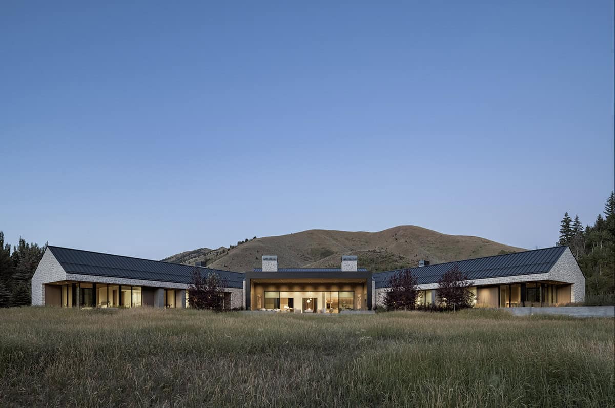 Dusk view of the symmetrical stone-and-glass home framed by rolling hills