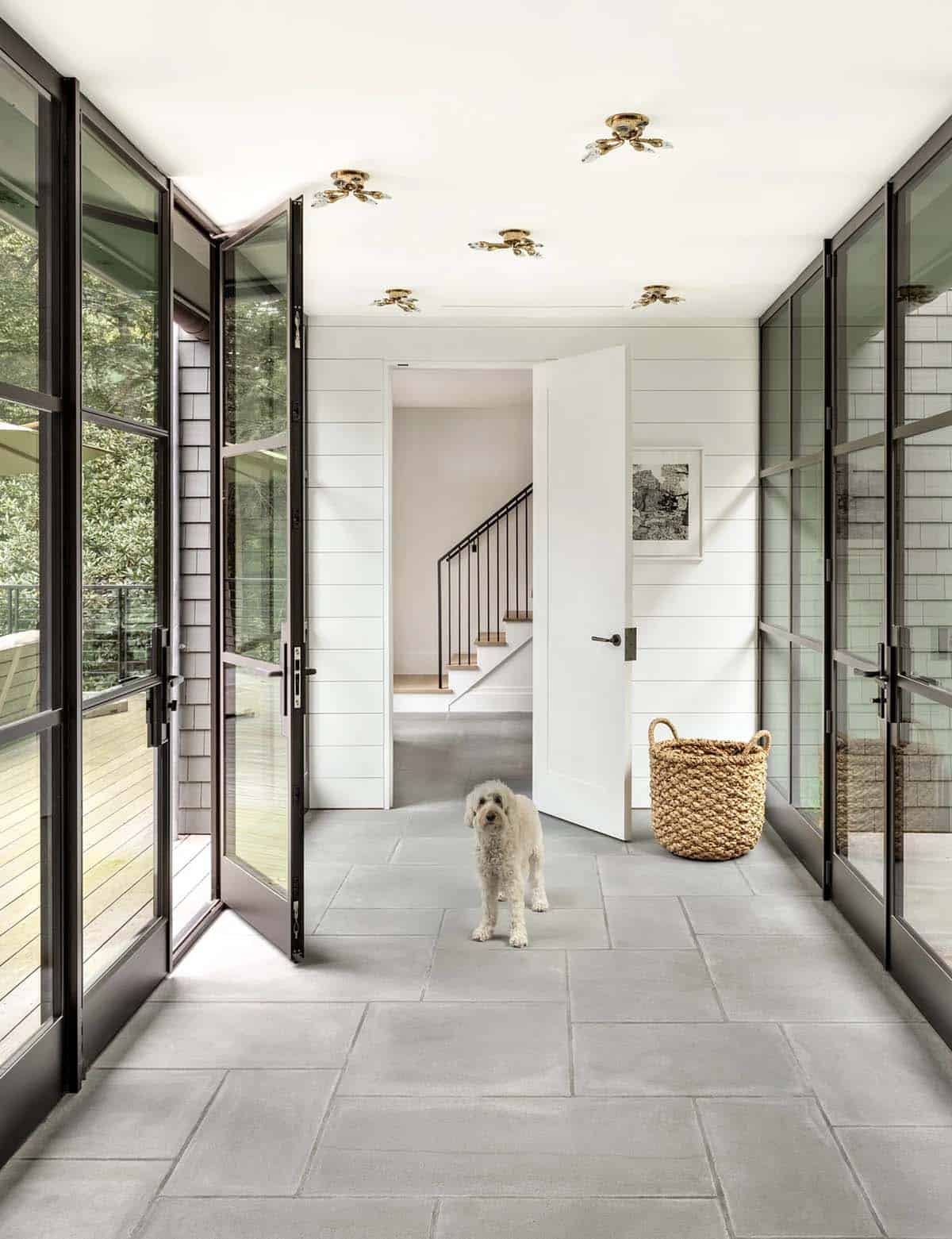 Bright glass-walled mudroom hallway with bluestone floor, dog standing near open white door to staircase