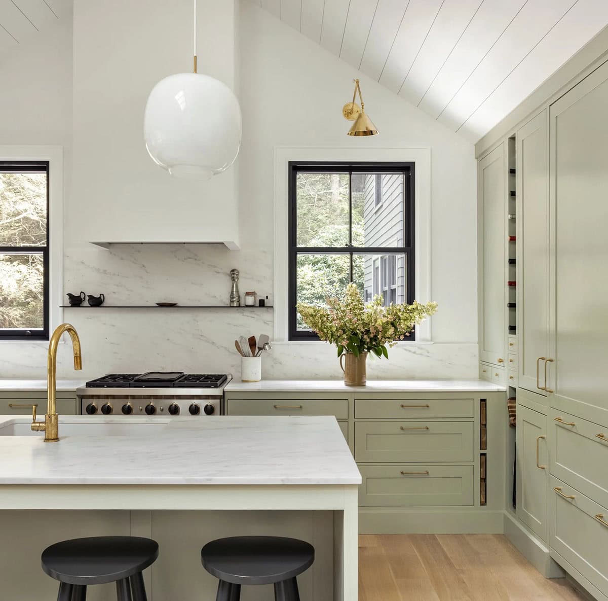 Kitchen with sage green cabinets, marble backsplash, vaulted shiplap ceiling, and brass fixtures