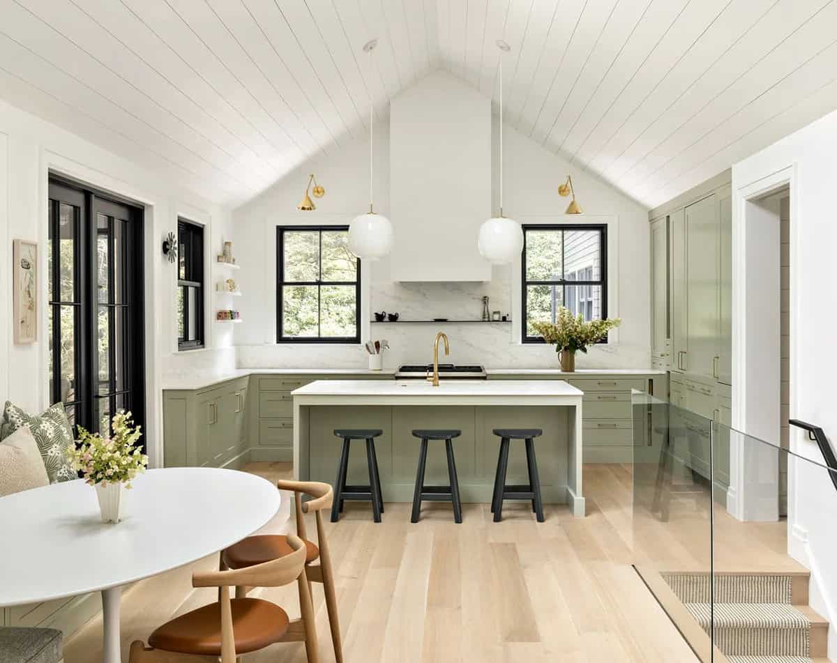 Wide view of sage green kitchen with island, black bar stools, and adjoining breakfast nook