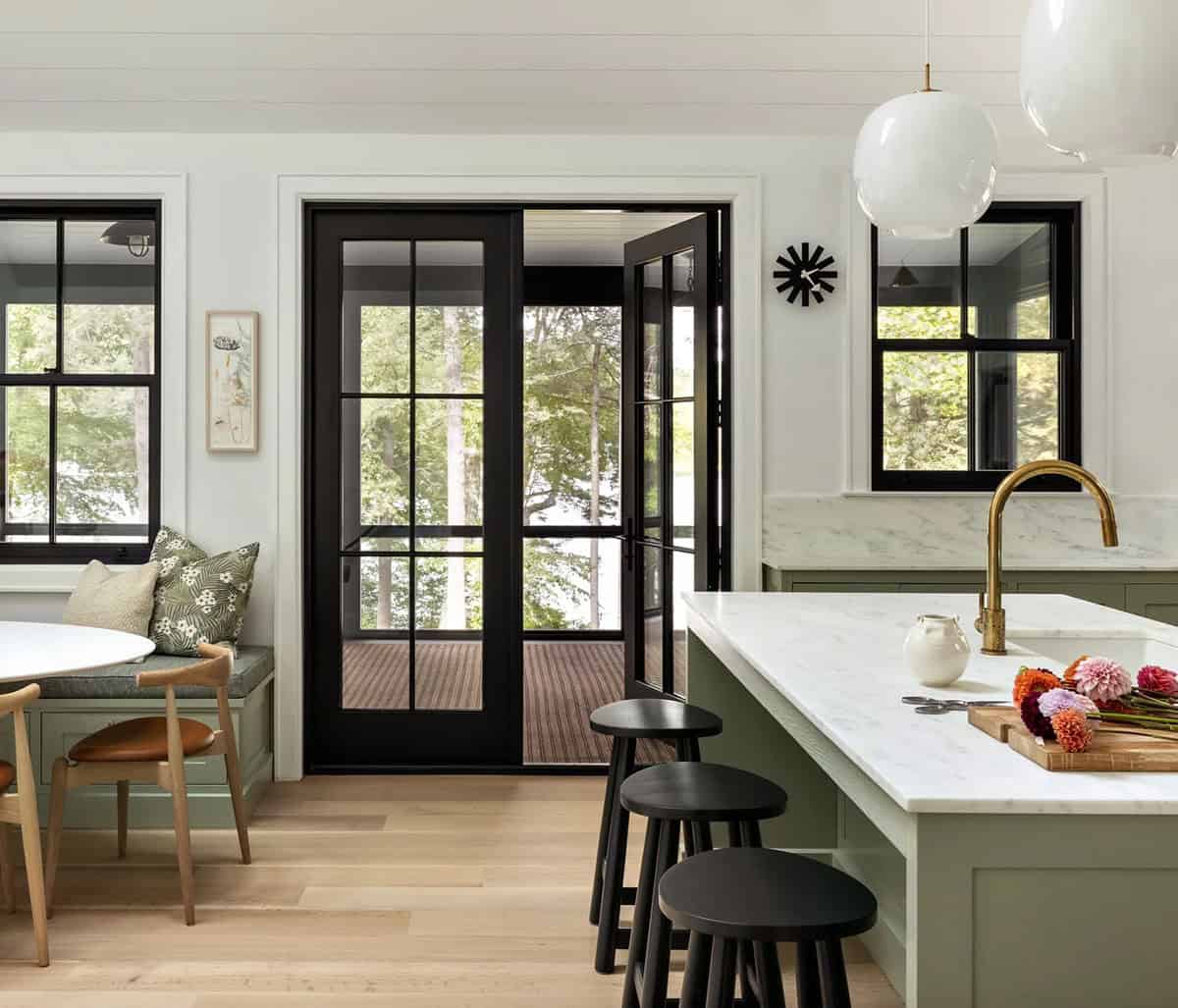 Kitchen island with marble counter and brass faucet, black French doors opening to screened porch