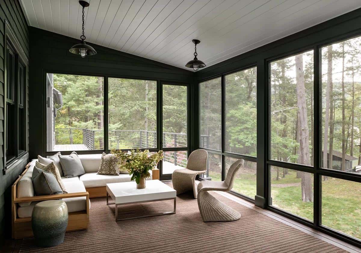 Screened porch with dark green walls, wicker chairs, white sectional sofa, and wooded view