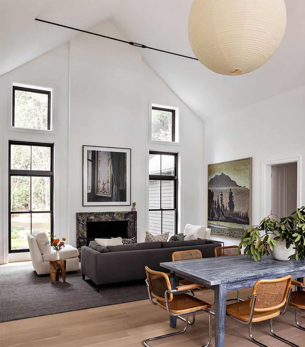 Living and dining area with stone fireplace, gray sofa, and tall pitched ceiling with windows