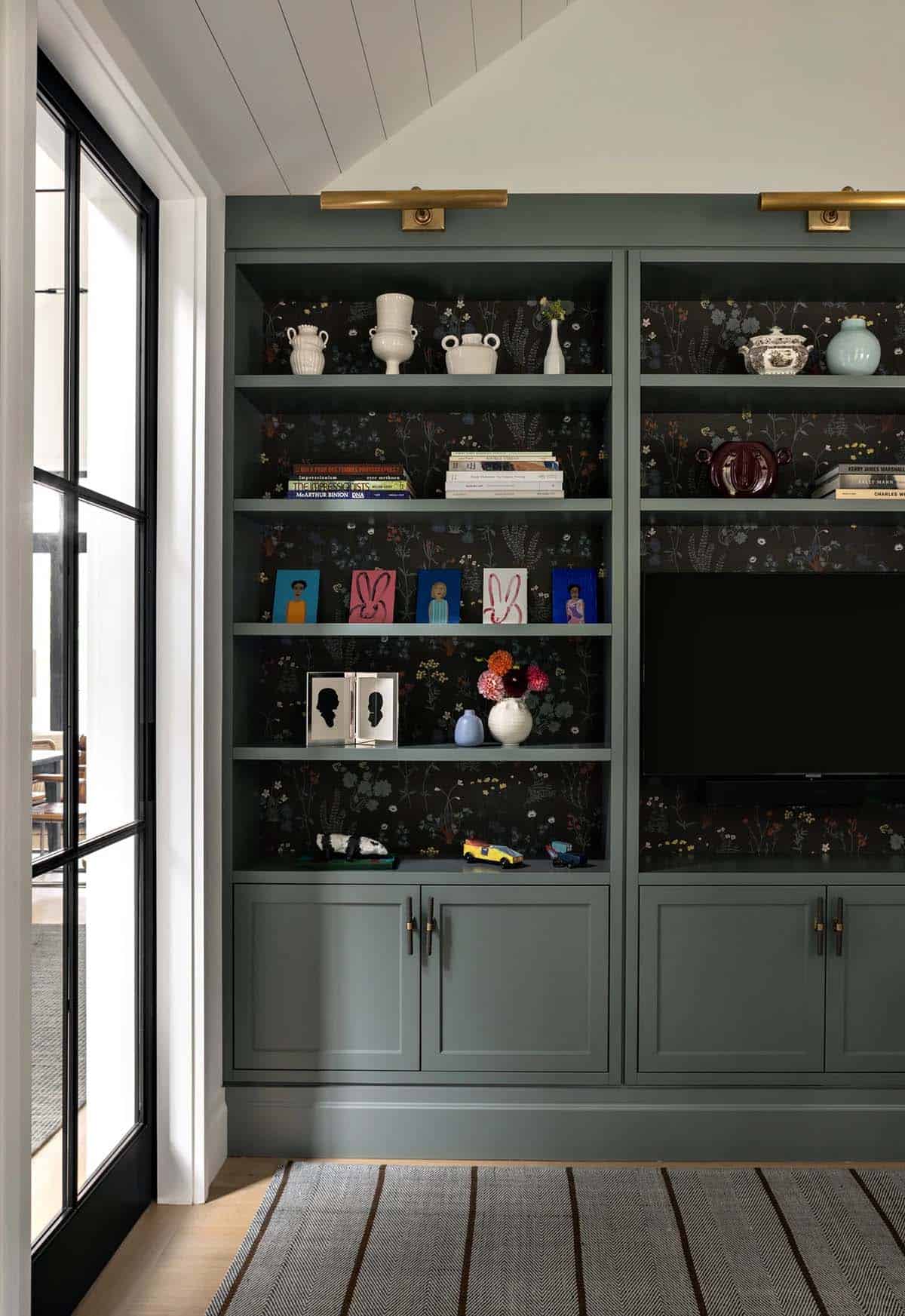 Built-in green shelving unit with floral wallpaper backing, displaying books, vases, and mounted TV