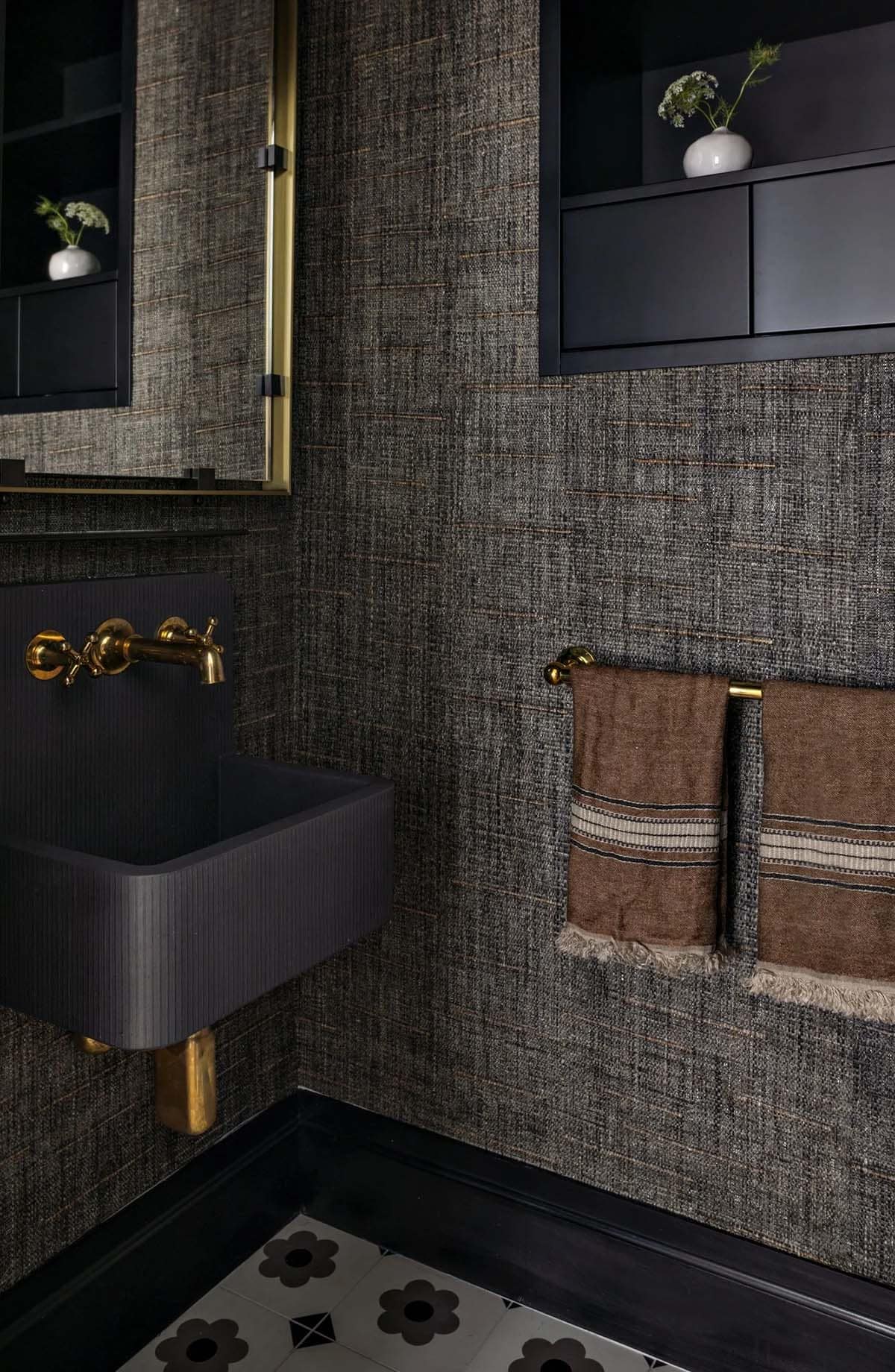 Moody powder room with textured dark grasscloth wallpaper, brass fixtures, and black wall-mounted sink