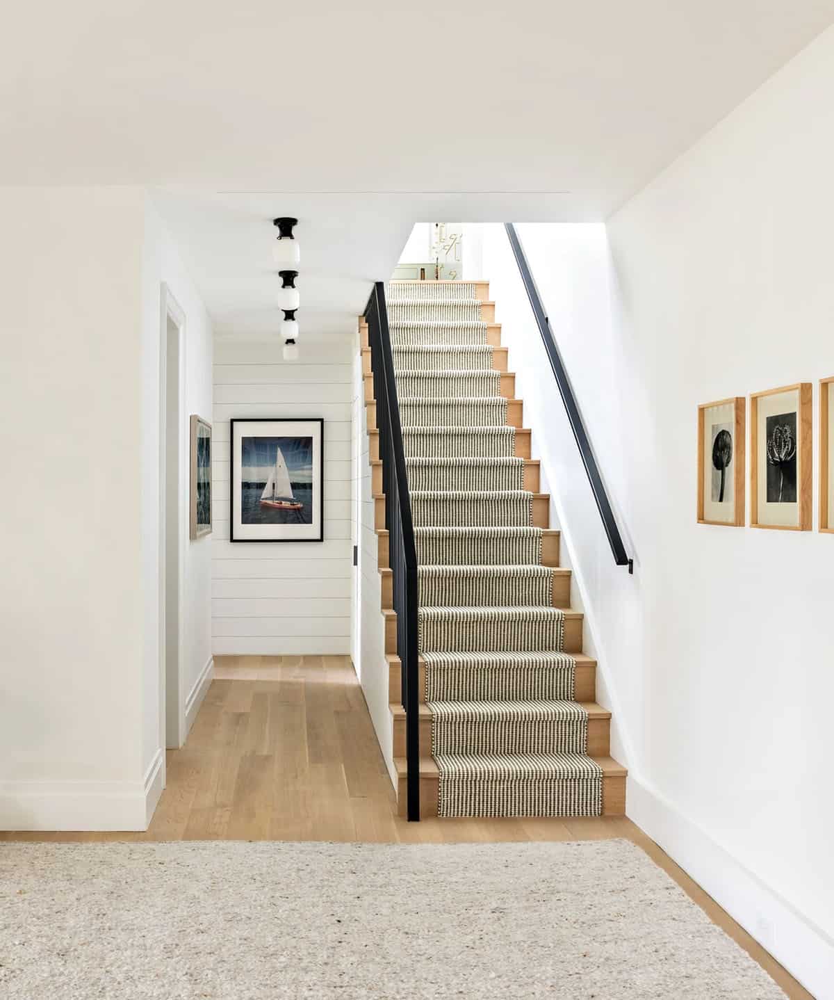 Staircase with striped runner and black railing, leading to hallway with framed art