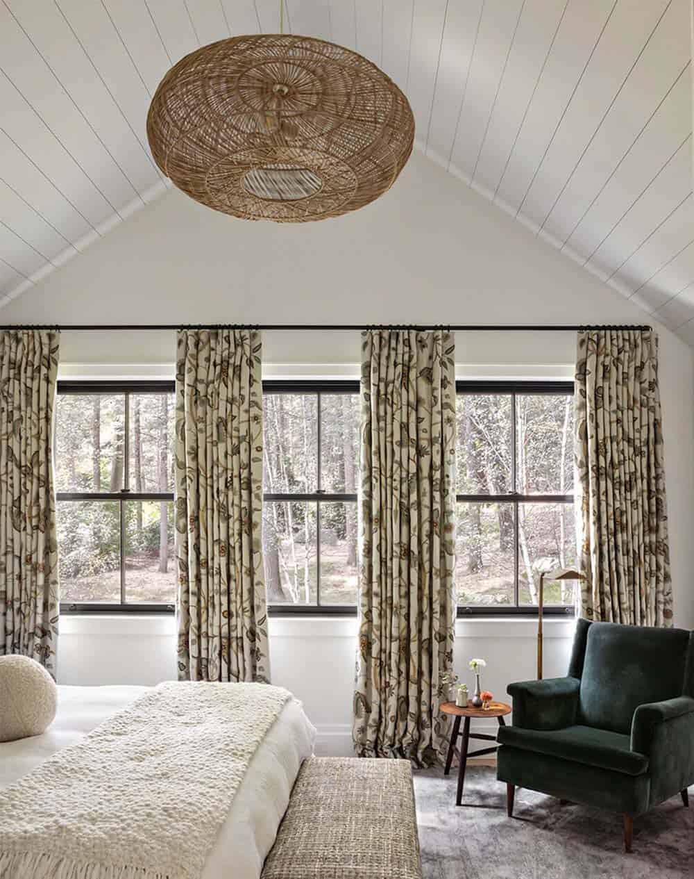 Bedroom with vaulted ceiling, woven pendant light, patterned curtains, and green velvet armchair