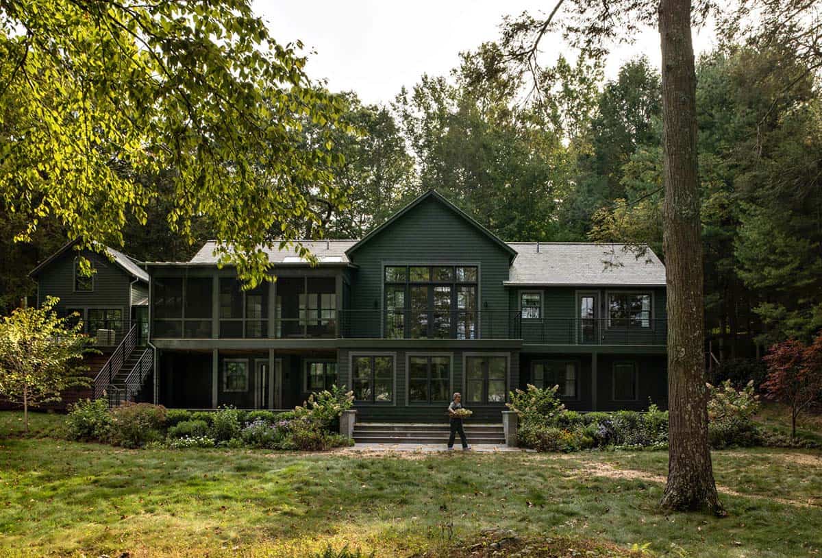 Rear facade of dark green two-story lake house with screened porch, balconies, and stone patio steps leading to lawn