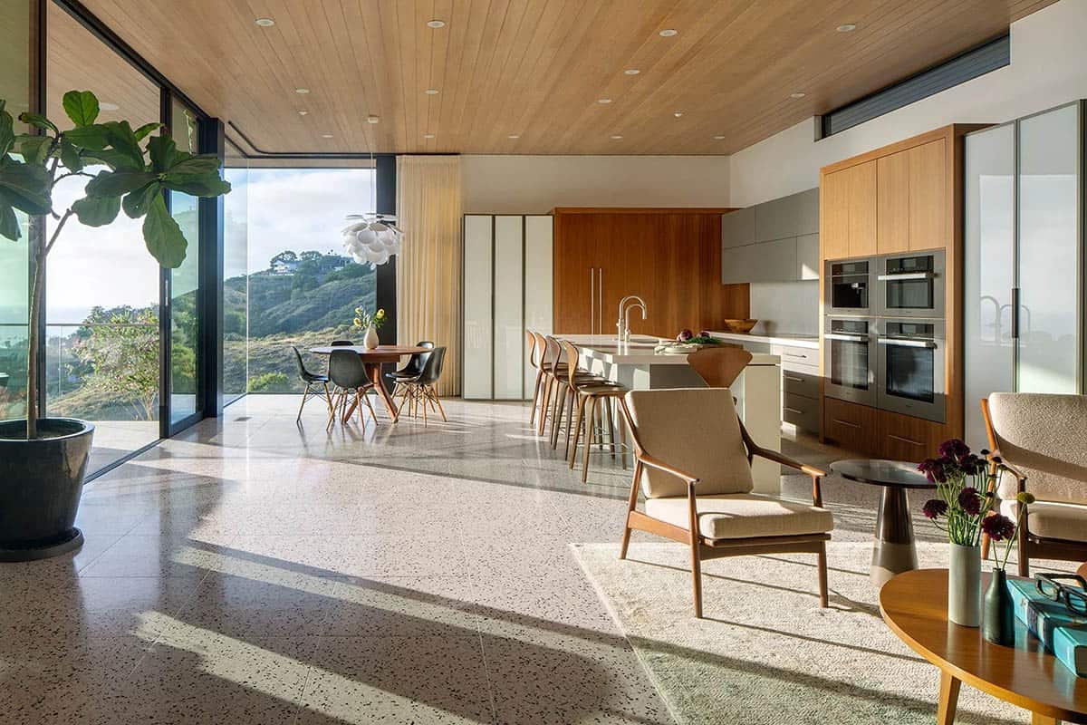 Bright open-plan kitchen and sitting area with floor-to-ceiling glass, freestanding island, and ocean views beyond