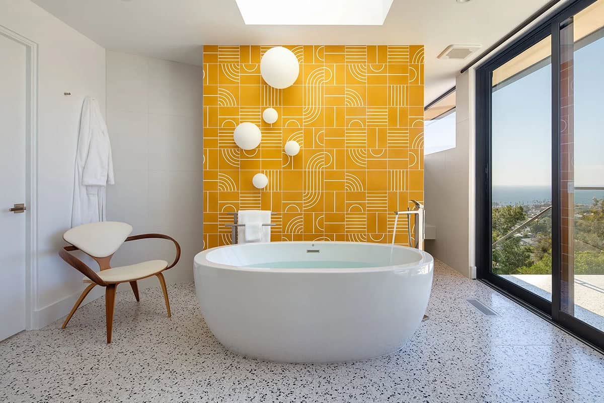 Primary bathroom with bold yellow geometric tile feature wall, oval freestanding soaking tub, skylight, and ocean views