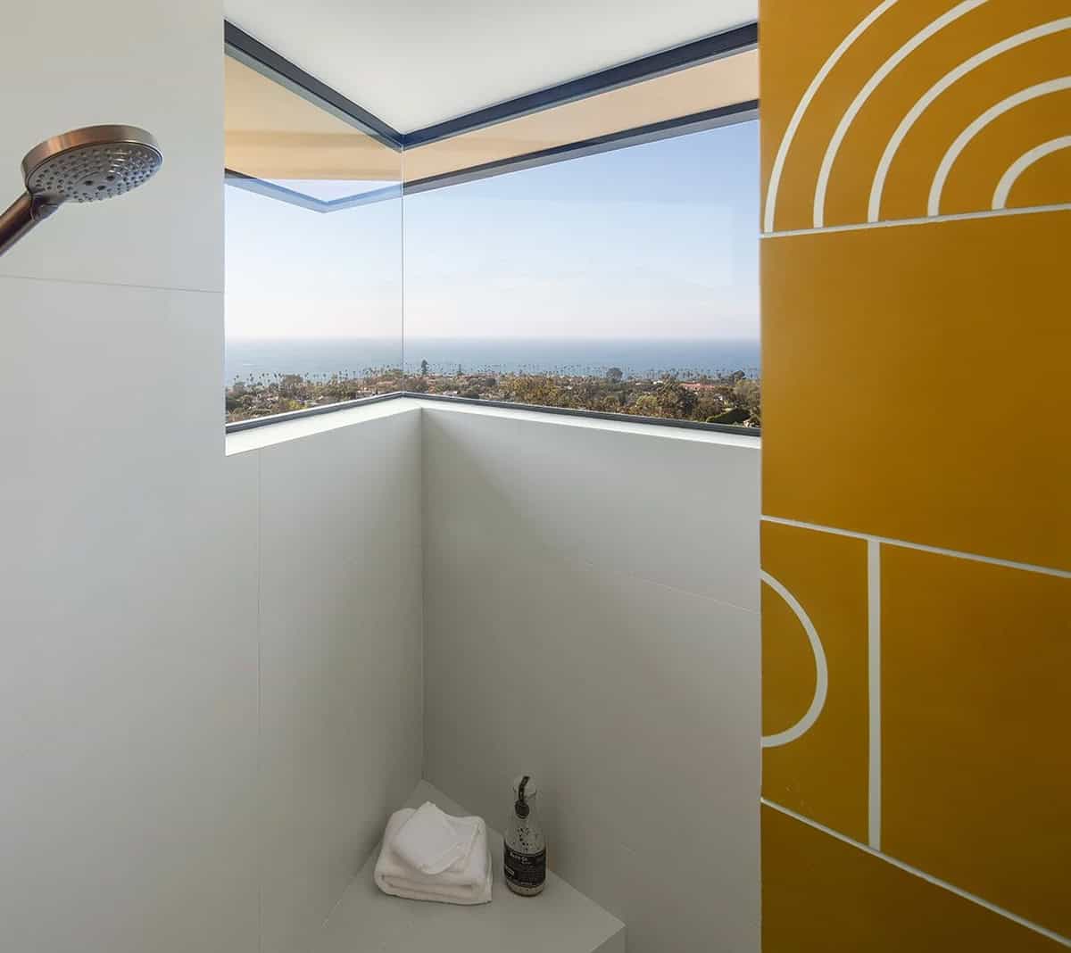 Frameless corner shower with floor-to-ceiling glass window overlooking treetops and Pacific Ocean