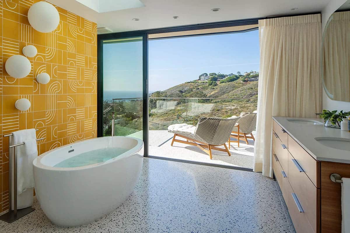 Primary bathroom with freestanding tub, mustard geometric tile wall, globe sconces, and open glass door to private terrace