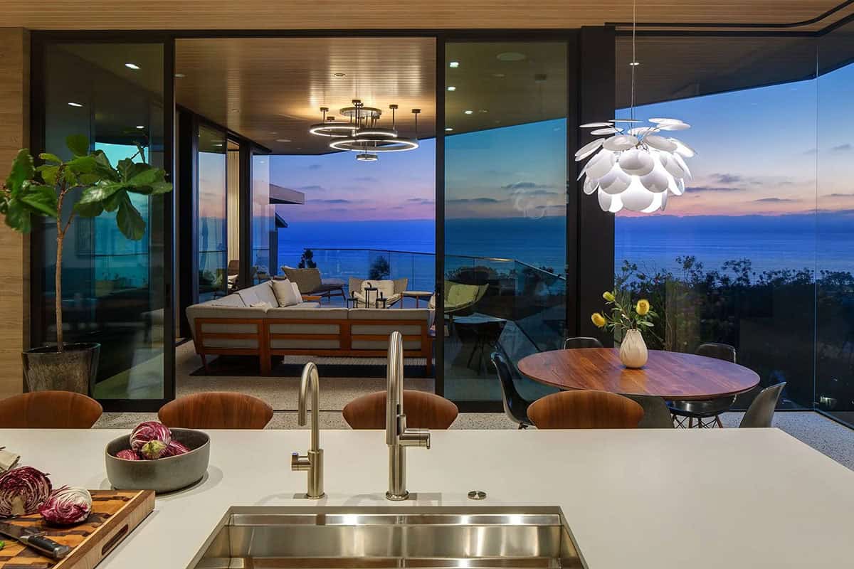 Kitchen island sink looking out through glass walls to covered terrace and glowing sunset over the ocean