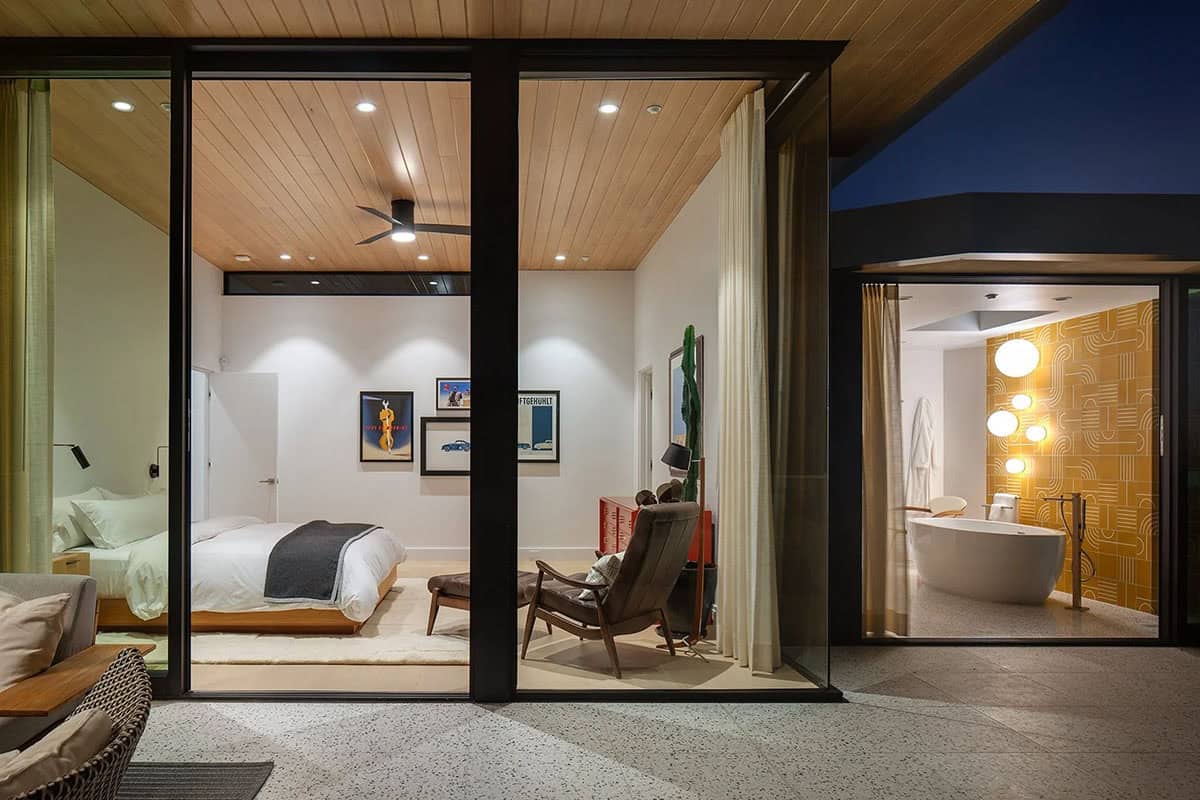 Nighttime exterior view of primary bedroom suite and ensuite bathroom through floor-to-ceiling glass sliding doors