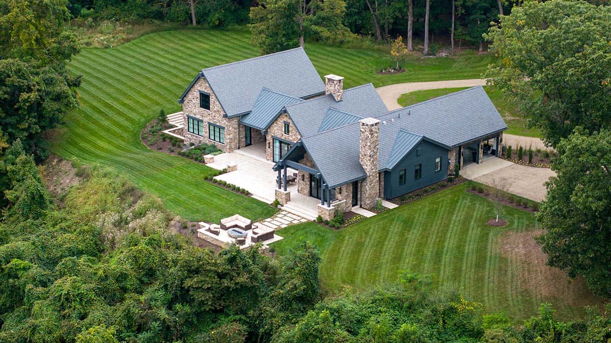 Aerial view of stone and metal-roofed modern mountain home in Pennsylvania surrounded by manicured lawn and trees