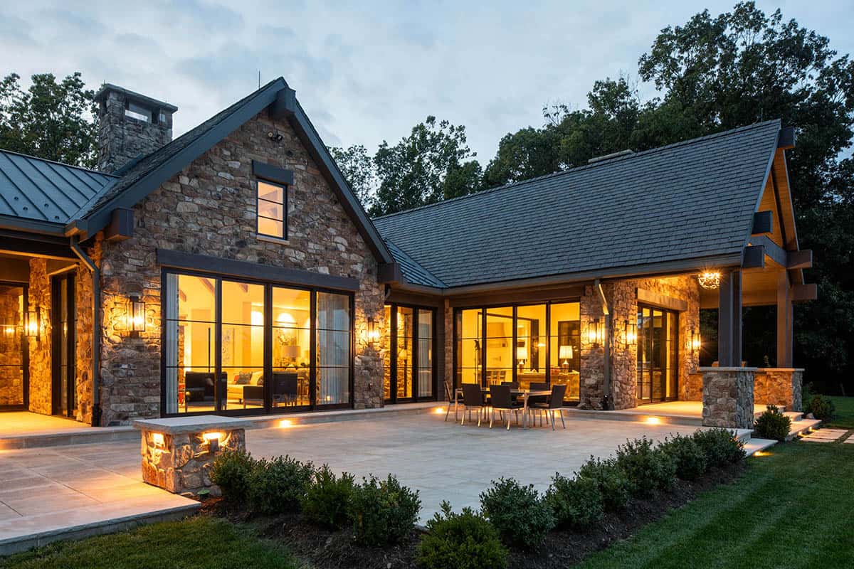 Stone mountain home exterior at dusk with glowing interior lights and covered patio with dining table