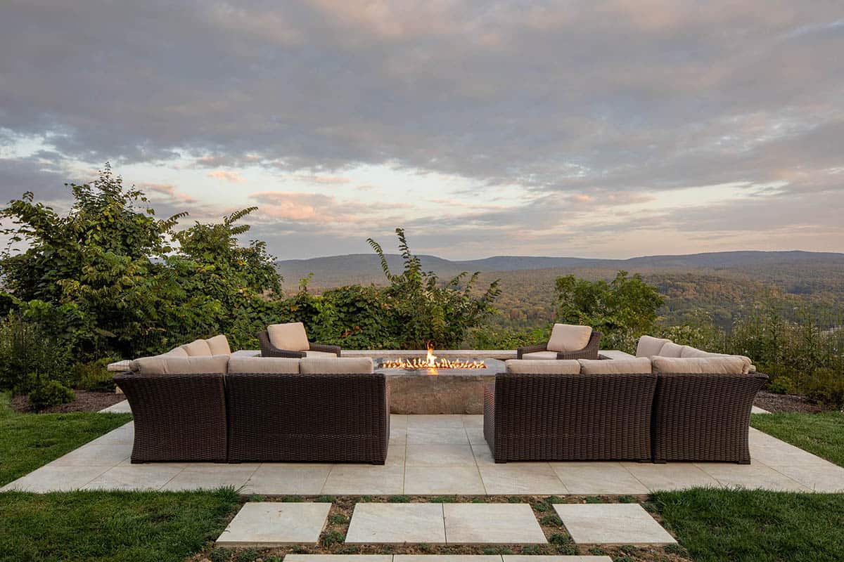 Outdoor fire pit with wraparound wicker seating overlooking layered mountain ridge views at sunset