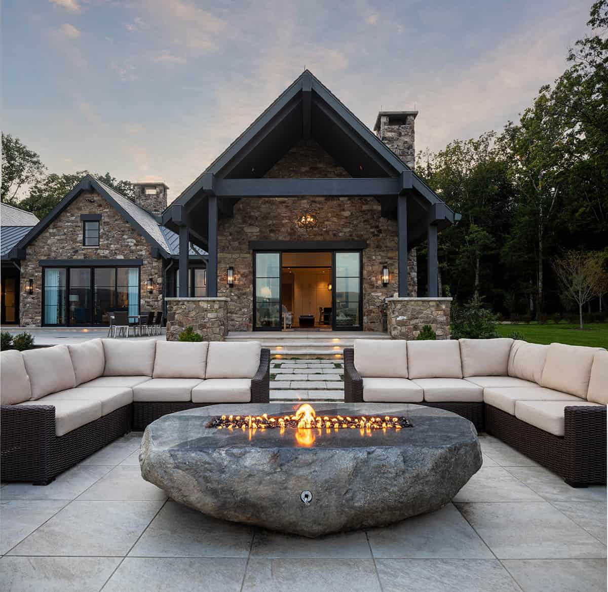 Natural boulder fire pit with cream sectional seating in front of stone gable and timber-framed porch