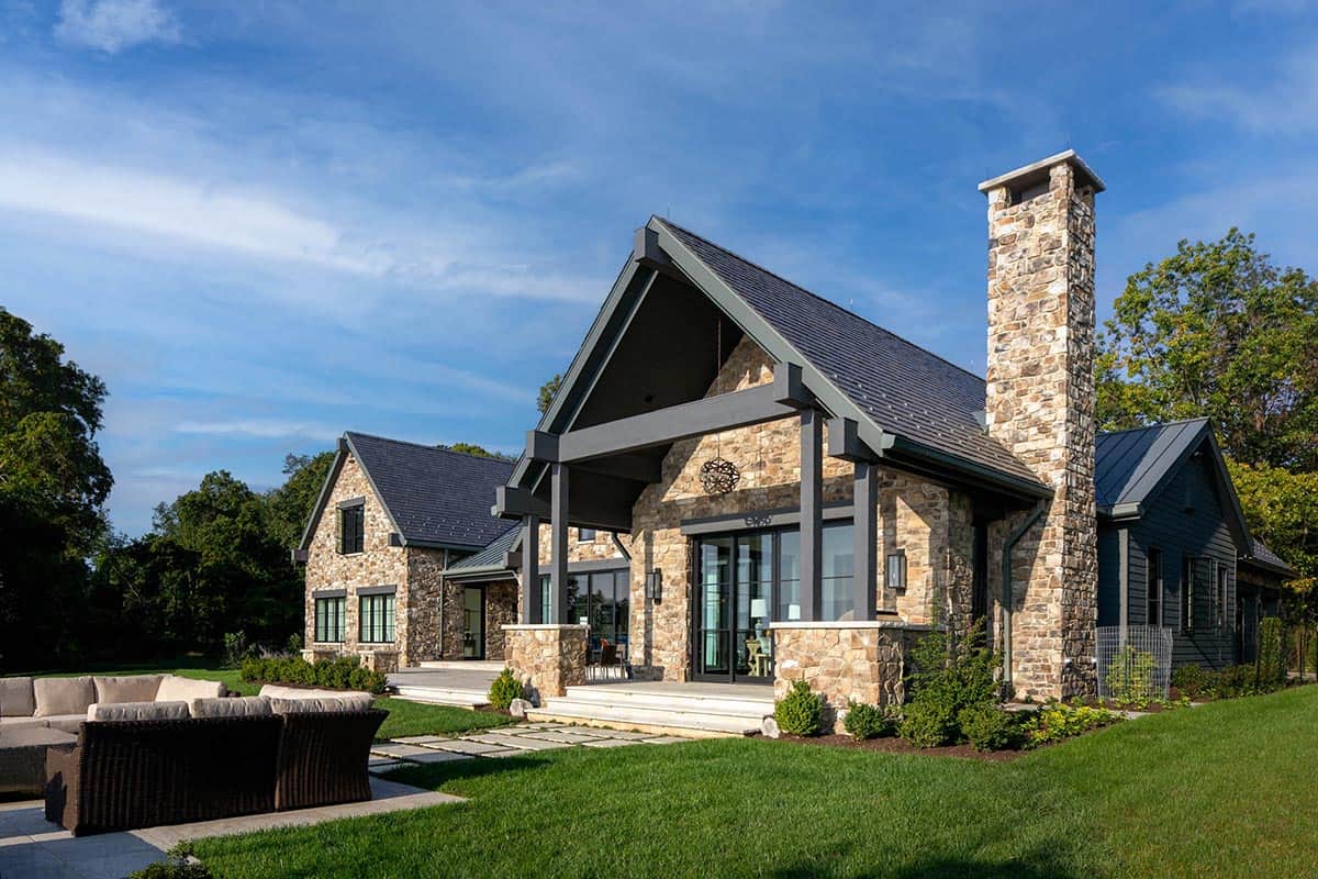 Stone gable exterior with tall chimney and timber-framed covered entry under a clear blue sky