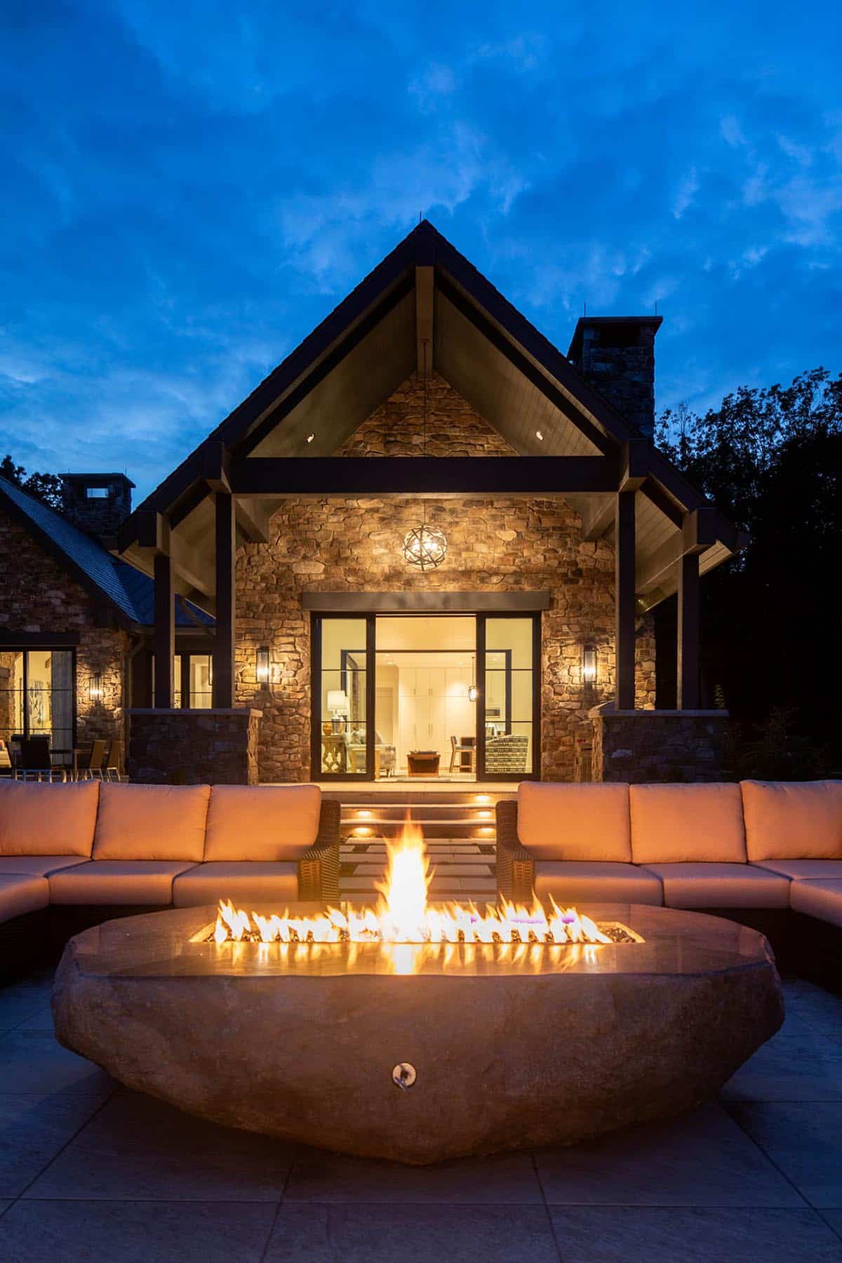 Stone gable facade illuminated at dusk with glowing fire pit and timber-framed porch overlook