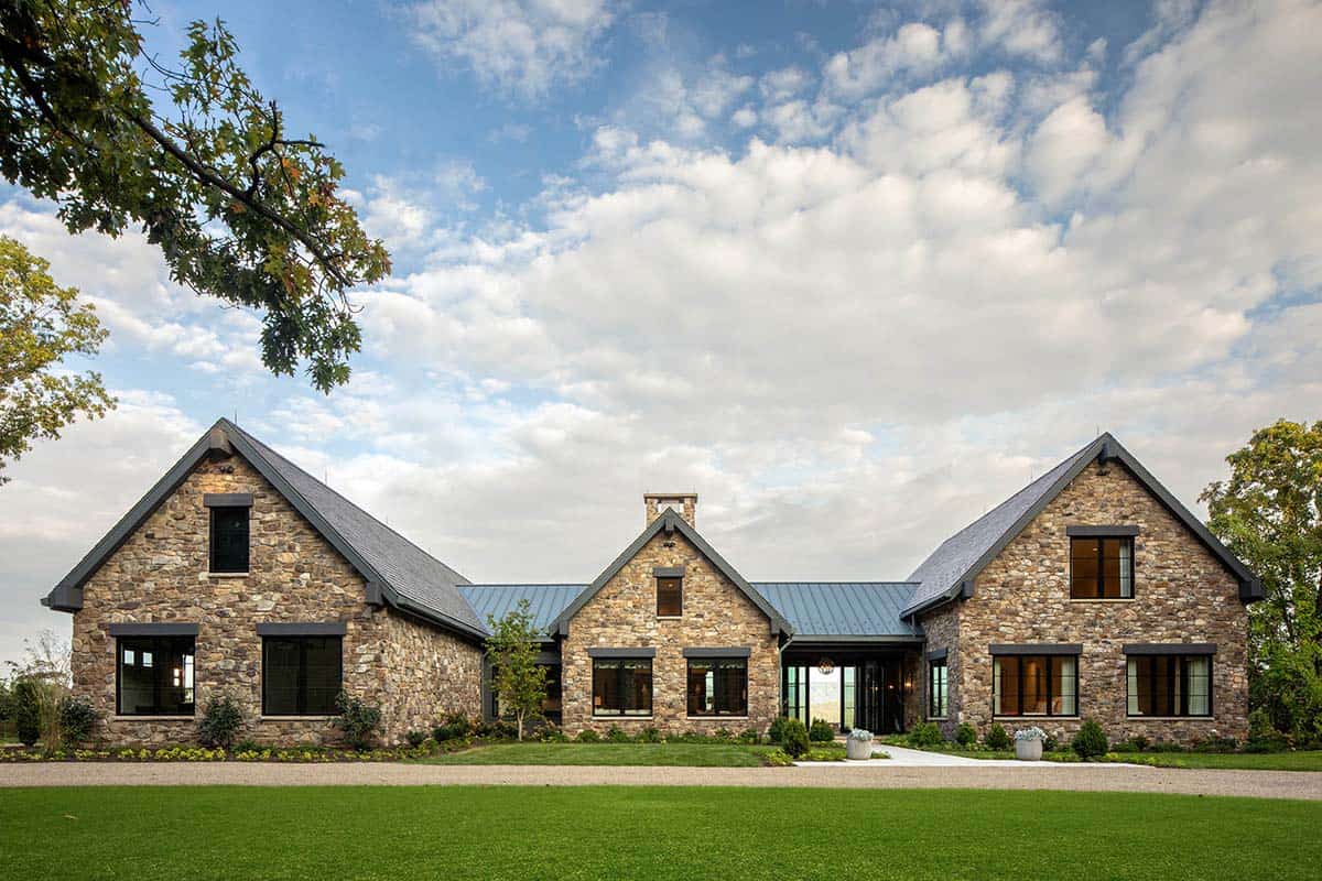 Front facade of stone mountain home with three gables and manicured lawn under a partly cloudy sky