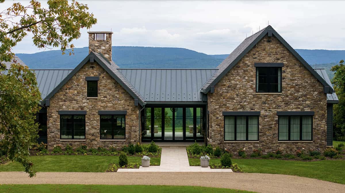 Stone home exterior with twin stone gables and a central chimney set against layered mountain ridges