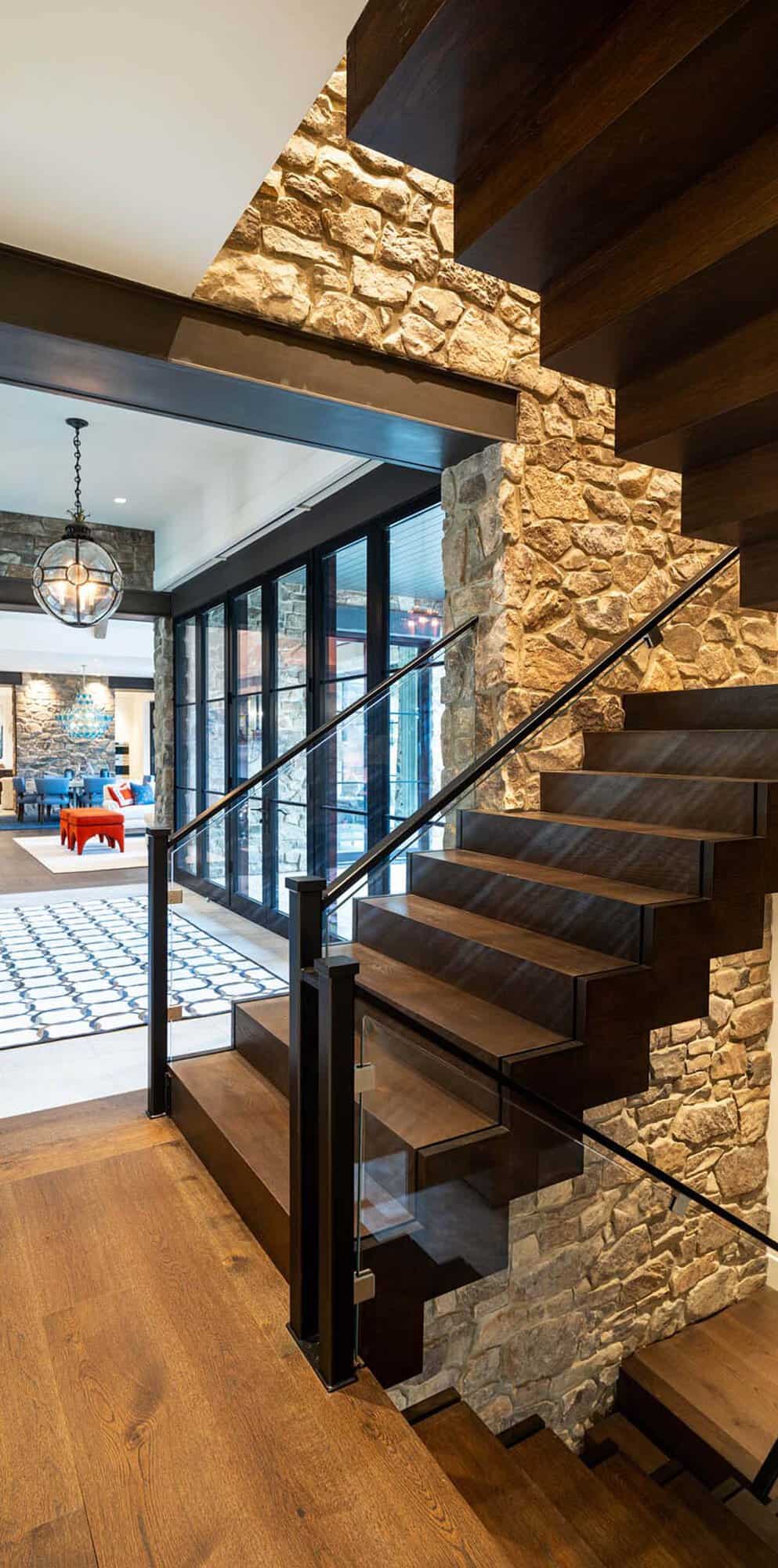 Floating wood staircase with glass railing built into a stone accent wall above an open living area
