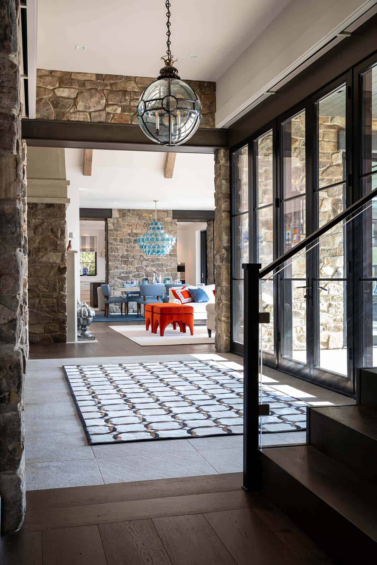 Stone-walled entry hallway with glass globe pendant light overlooking patterned rug and living room beyond