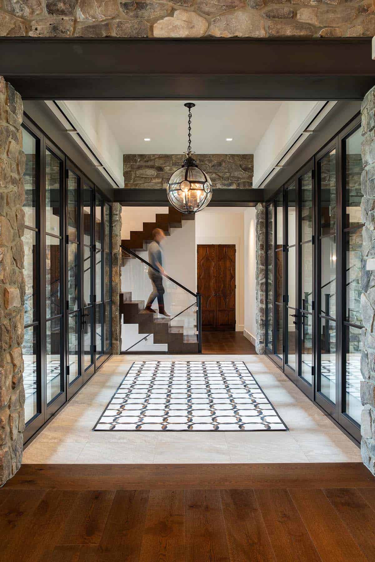 Glass-walled stone entry corridor with globe pendant light and floating staircase in the background