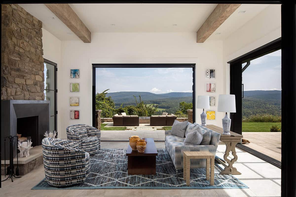 Living room with stone fireplace and patterned furnishings opening to a sweeping mountain view through glass doors