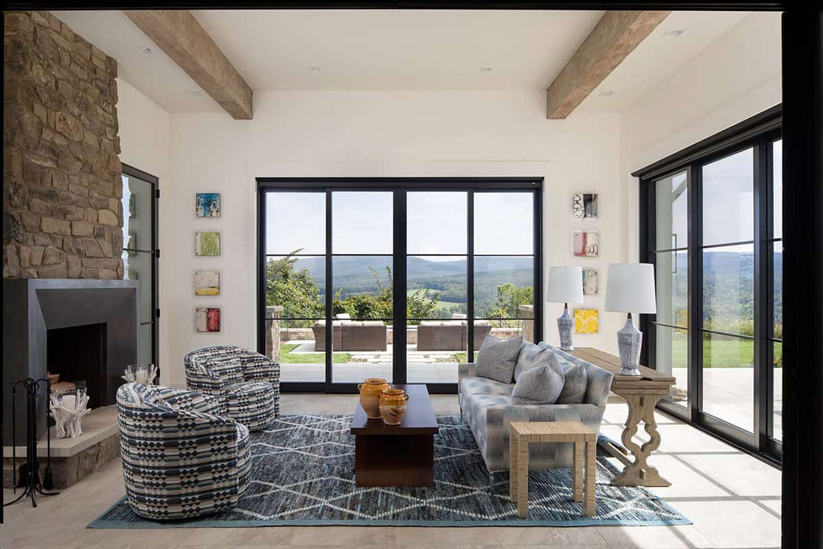 Living room with stone fireplace, patterned swivel chairs, and sliding glass doors framing mountain views