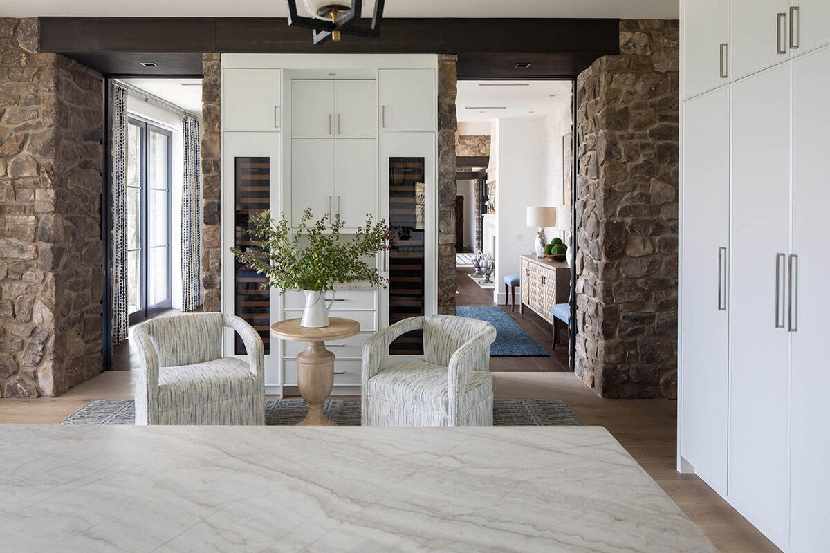 Cozy seating nook with patterned armchairs, round side table, and built-in wine refrigerators flanked by stone columns