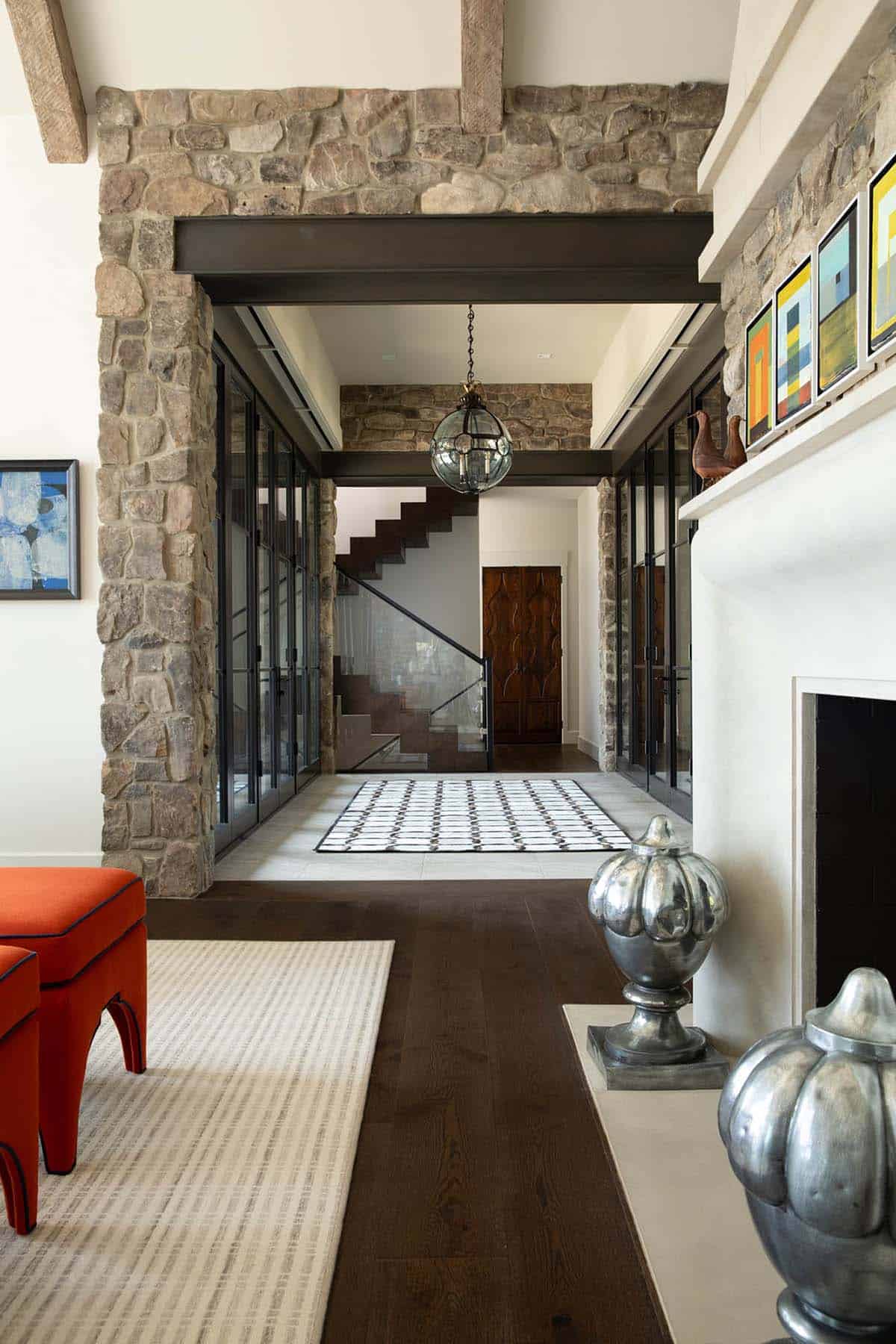 Stone-walled hallway with glass doors and floating staircase, framed by an orange ottoman and fireplace nook