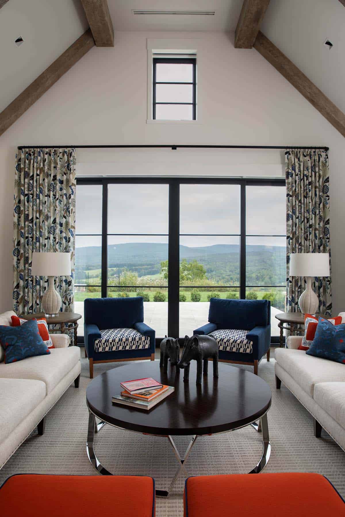 Living room with cream sofas, navy velvet chairs, and floral drapes framing glass doors to a mountain view