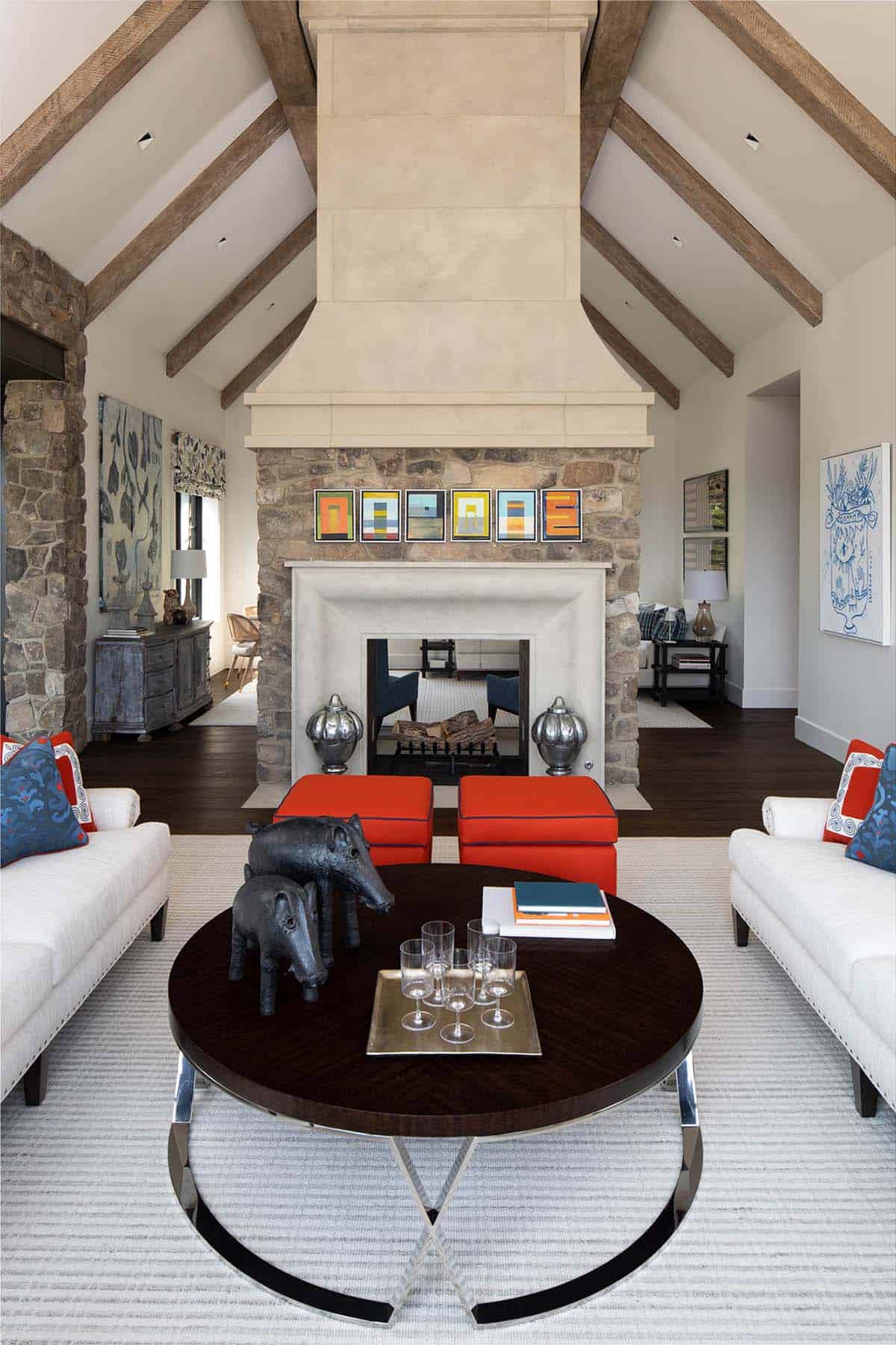 Vaulted living room with stone fireplace, carved wood mantel, and cream sofas accented in red and blue
