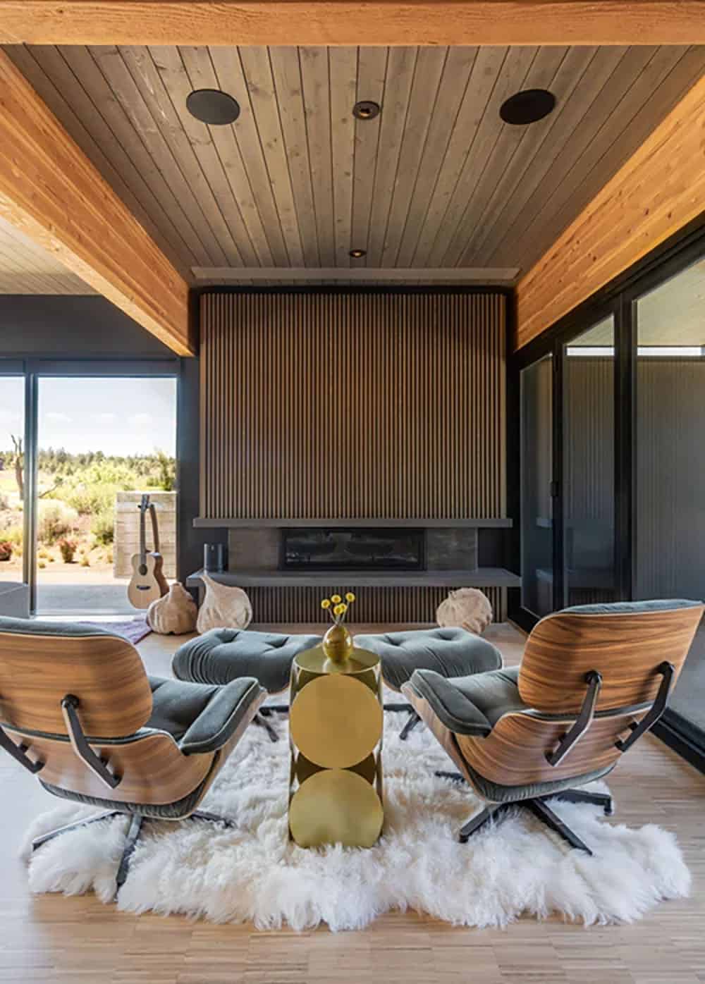 Two Eames lounge chairs on white sheepskin rug facing a linear fireplace with vertical wood slat surround