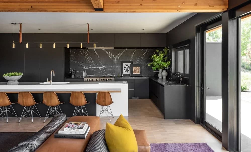 Dark kitchen with matte black cabinets, black marble backsplash, white island with wood bar stools, and pendant lighting