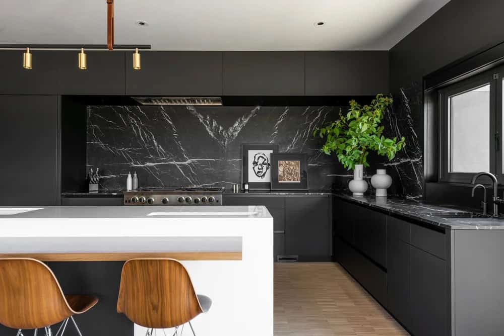 Black kitchen with marble backsplash, white island, walnut bar stools, and brass pendant lights